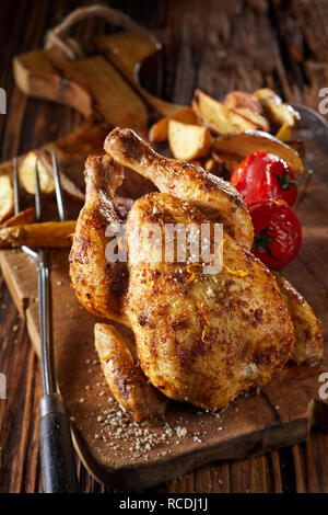 Poussin grillé ou très jeune poulet printemps servi entier sur une planche en bois avec des quartiers de pommes de terre et tomates Banque D'Images