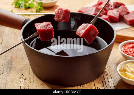 Bœuf frais crus sur les fourchettes à fondue prêt pour plonger dans l'huile chaude dans une vue en gros plan avec des côtés Banque D'Images