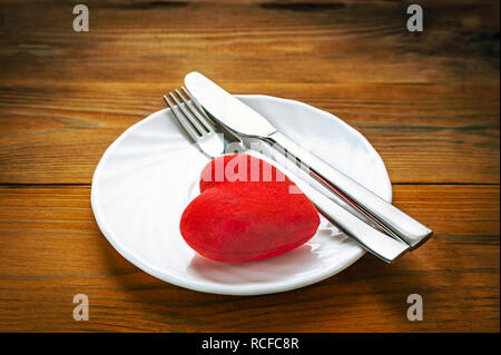 Peluche coeur rouge avec fourchette et couteau en terminé le repas Position sur une plaque blanche. Fond de bois. Santé, minimaliste Liquidation Symbole. Carte, moi Banque D'Images