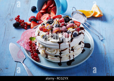 Des Pavlova dessert avec des couches de meringue et de crème fouettée surmontée d'un assortiment de fruits de saison et le zeste d'orange arrosées de cho Banque D'Images