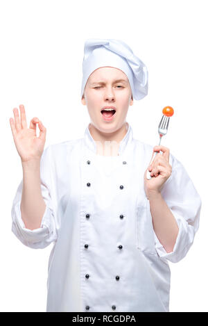 Chef dans un bouchon avec tomate sur une fourchette montre un geste de la main sur un fond blanc Banque D'Images