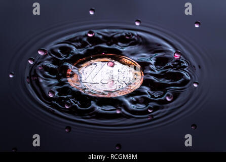 Couleur rouge goutte d'eau éclaboussant sur un Euro et sterling coin étang anglais Banque D'Images