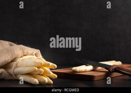 Asperges fraîchement récoltées dans un sac de jute sur une planche à découper en bois Banque D'Images