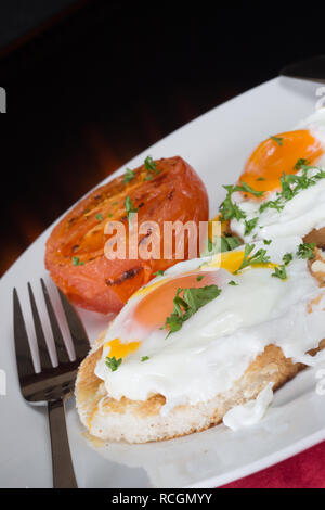 Un petit-déjeuner anglais de l'œuf poché sur plaque beurrée avec tomates grillées Banque D'Images