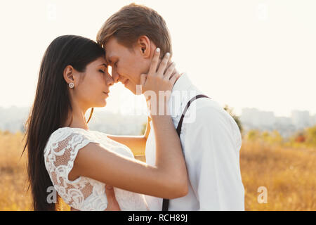 Couple aimant habillé en blanc, prêt à baiser en plein air avec les yeux fermés, toucher doux, l'autre avec un paysage flou en arrière-plan, golden gr Banque D'Images