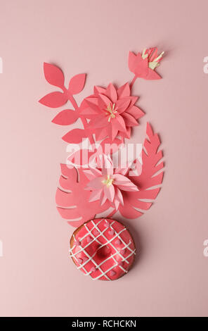 Donut rose avec du glaçage et origami papier décor fleurs modernes, sur fond rose, monochrome close up Banque D'Images