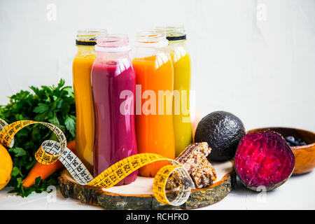 Rouge, orange, vert et jaune, jus, smoothies frais bouteilles avec des verts et des frutis,bande mesure et muesli bars, en bonne santé, mode de vie végétalien concept Banque D'Images