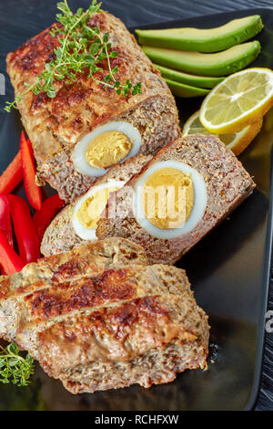 Viande farcies d'œufs servis avec red bell peppe, citron et de tranches d'avocat sur un plateau rectangulaire noir sur une table de bois, vue verticale d'en haut Banque D'Images