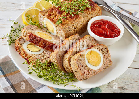 Viande farcies avec oeuf dur servi avec une sauce tomate et des rondelles de citron sur une plaque blanche sur une vieille table en bois, vue de dessus, close-up Banque D'Images