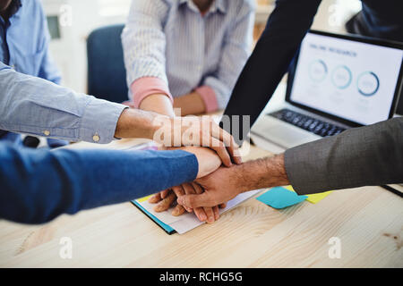 Young businesspeople sitting around table dans un bureau moderne, mettant les mains ensemble. Banque D'Images