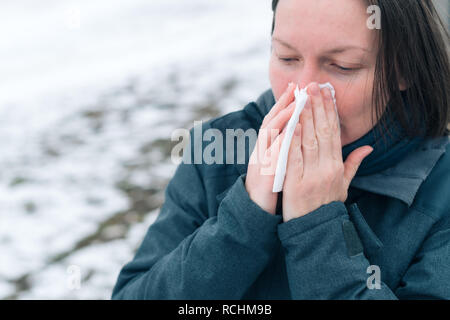 Libre de son nez dans le mouchoir en papier dans la rue par une froide journée d'hiver au début de la saison de la grippe Banque D'Images