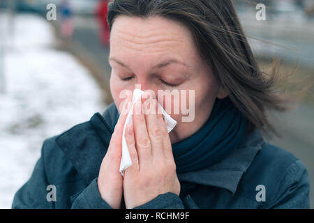 Libre de son nez dans le mouchoir en papier dans la rue par une froide journée d'hiver au début de la saison de la grippe Banque D'Images