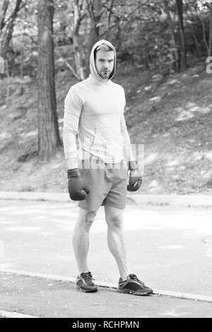 Grand jour arrive. Athlète homme concentré sur le visage avec des gants de boxe sport pratique prêt punch fond nature. Boxer hooded motivé pour réussir. Boxer sportif formation avec des gants de boxe. Banque D'Images