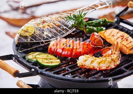 Barbecue d'hiver avec des fruits de mer raffinés au cours de la cuisson des charbons ardents, dont une queue de homard, poissons entiers et de saumon assaisonné avec des herbes Banque D'Images