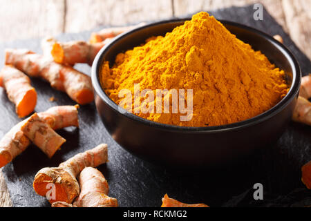 Le curcuma bio en poudre dans un bol et la racine fraîche sur la table horizontale. Banque D'Images