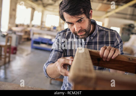 Fabricant de meubles travaillant sur une chaise dans son grand atelier Banque D'Images