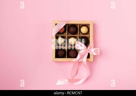 Un ensemble de différents chocolats dans une boîte de papier avec un ruban rose satiné brillant sur un fond bleu. Place pour la conception. Télévision mise en page. Concept de fête. Cop Banque D'Images