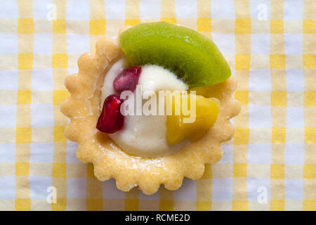 M&S mini tarte aux fruits avec kiwi, ananas et graines de grenade situé sur jaune et blanche serviette serviette vérifié Banque D'Images