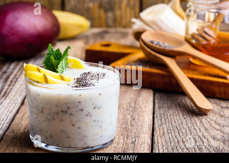 Smoothie banane mangue en verre, dessert sain naturel avec du yaourt grec et chia seeds, petit déjeuner végétarien avec du miel sur la table en bois, clos rural Banque D'Images