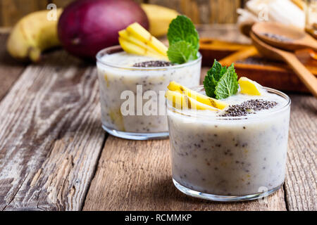 Smoothie banane mangue en verre, dessert sain naturel avec du yaourt grec et chia seeds, petit déjeuner végétarien avec du miel sur la table en bois, clos rural Banque D'Images