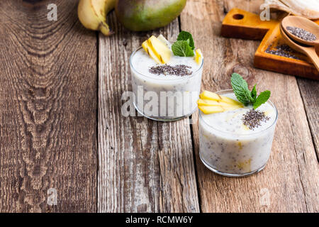 Smoothie banane mangue en verre, dessert sain naturel avec du yaourt grec et chia seeds, petit déjeuner végétarien avec du miel sur la table en bois, clos rural Banque D'Images