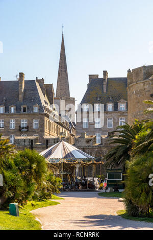 Un carrousel de style vintage à Saint-Malo en Bretagne, France, avec le clocher de la cathédrale Saint-Vincent coller dehors au-dessus des bâtiments au coucher du soleil. Banque D'Images