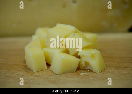 Gros plan du Dutch des cubes de fromage avec des trous, sur une planche à découper en bois, avec une plus grande roue de fromage montrant en arrière-plan. Banque D'Images