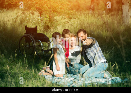 Famille heureuse de prendre le pique-nique sur selfies en parc. Paraplegic Banque D'Images