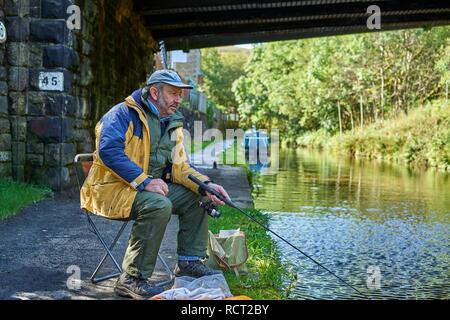 L'homme, assis, la pêche Huddersfield canal étroit, Marsden, West Yorkshire, Angleterre Banque D'Images