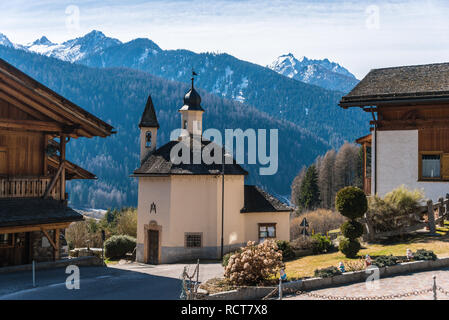 Petite chapelle, l'église de montagne italien entre les maisons avec des montagnes enneigées à l'arrière-plan. Claiano di Pell, Trentino, Trento, Italie Banque D'Images