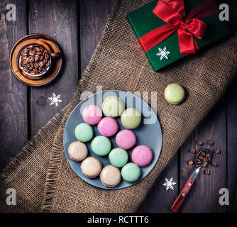 Macarons colorés dans la plaque bleue près de tasse de café et d'aujourd'hui fort de Noël sur fond de bois Banque D'Images