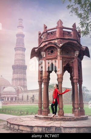 Femme en costume rouge avec écharpe, debout près de l'architecture ancienne de Qutub Minar tour dans la vieille ville de Delhi, Inde Banque D'Images