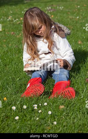 Petite fille assise sur l'herbe et la lecture d'une bande dessinée Banque D'Images