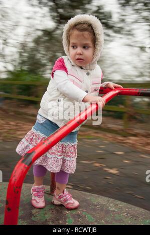 Jeune fille, trois ans, jouant sur l'aire de rond-point Banque D'Images