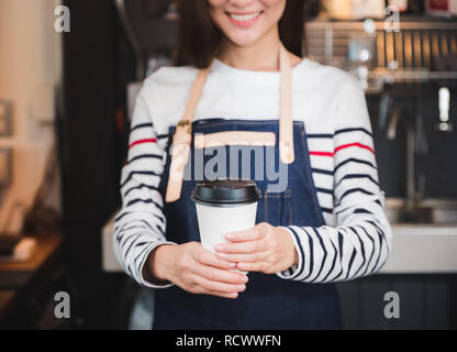 Asian woman holding tablier barista jean porter la tasse de café chaud servi au client avec smiling face au comptoir du bar, café restaurant service concept.waitres Banque D'Images