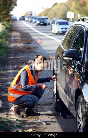 Panne de voiture, la conductrice s'est arrêtée sur la bande d'arrêt d'une route de campagne portant un gilet réfléchissant Banque D'Images