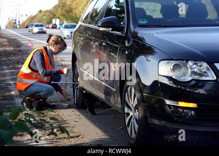 Panne de voiture, la conductrice s'est arrêtée sur la bande d'arrêt d'une route de campagne portant un gilet réfléchissant Banque D'Images