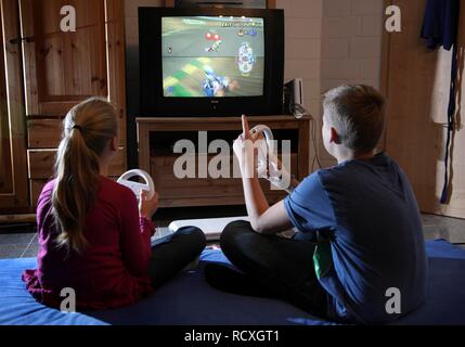 Frères et sœurs, un garçon, 12 ans, et une fille, 10 ans, de jouer à un jeu de course de voiture sur une Wii console de jeux dans leur chambre ensemble Banque D'Images