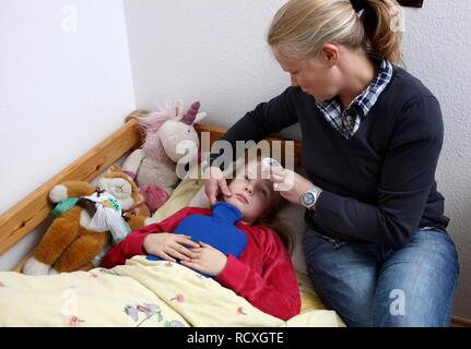 Fille, 10 ans, est malade au lit avec un rhume, grippe, fièvre, sa mère de prendre la température avec un thermomètre de la peau numérique Banque D'Images