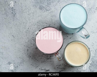 Des boissons à la mode : bleu, jaune et rose latte. Vue de dessus du papillon bleu chaud du pois ou la spiruline latte, jaune ou or rose curcuma latte et latte de betteraves rouges sur fond de ciment gris. L'espace de copie pour le texte Banque D'Images