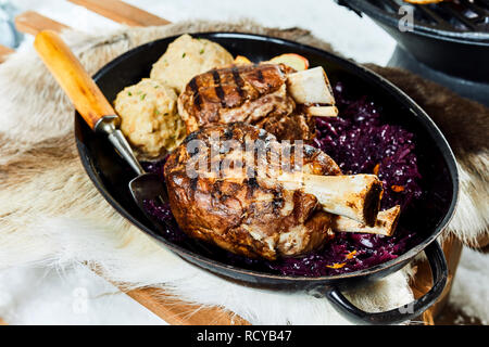 Barbecue d'hiver avec des jarrets de porc grillé servi avec du chou rouge et de raviolis pour une cuisine traditionnelle Allemande sur un fond de neige Banque D'Images