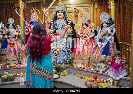 L'ARTI rituel. Une pieuse femme hindoue prie et vagues feu devant des statues des divinités dans un temple dans le Queens, New York. Banque D'Images