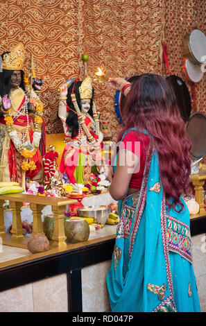 L'ARTI rituel. Une pieuse femme hindoue prie et vagues feu devant des statues des divinités dans un temple dans le Queens, New York. Banque D'Images