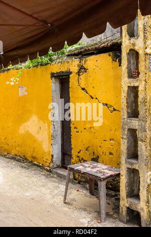 À côté des selles jaune lumineux délabré vieux bâtiment à côté de la porte et sous un auvent à Hoi An, Vietnam Banque D'Images