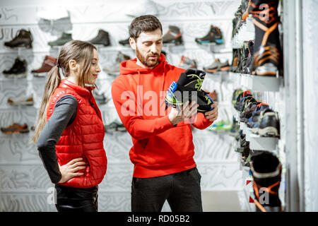 L'homme et la femme à la recherche sur les chaussures à crampons pour la randonnée sur la glace debout dans le magasin de sport moderne Banque D'Images