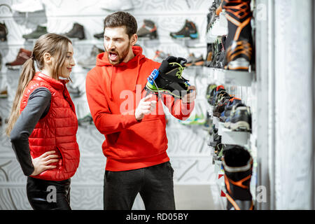 L'homme et la femme à la recherche sur les chaussures à crampons pour la randonnée sur la glace debout dans le magasin de sport moderne Banque D'Images