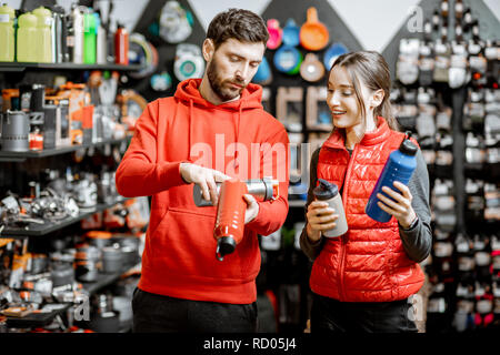 Jeune couple vêtu de rouge sportswear choisissant la vaisselle pour le camping dans la boutique avec l'équipement de voyage Banque D'Images