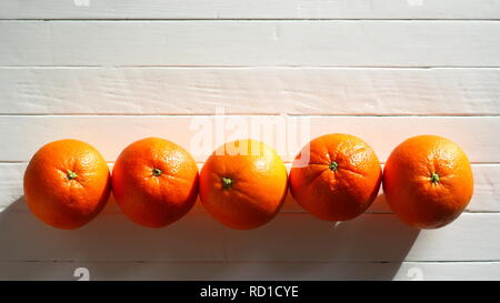 Les oranges, cinq sur une ligne sur une vieille table en bois blanc, il en lumière du soleil Banque D'Images