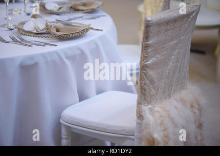 Élégamment couverts chaise avec tissu beige nacré métal et plumes et le restaurant la table, pour un dîner raffiné Banque D'Images