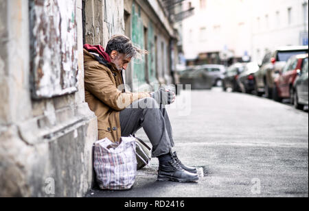 Les sans-abri mendiant homme assis à l'extérieur en ville pour demander de l'argent don. Banque D'Images